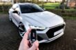 Close-up of a hand holding a car key fob with an RS emblem, in front of a white sport sedan.